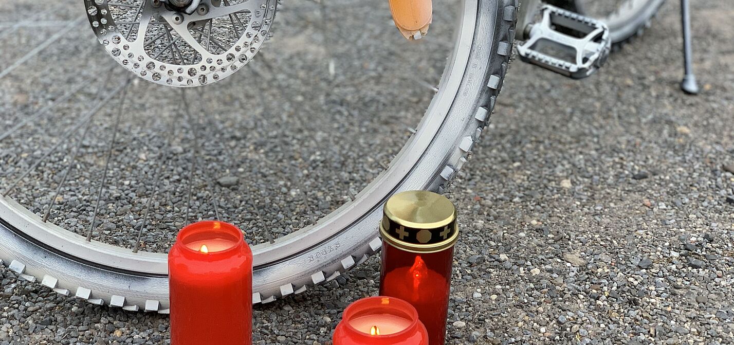 Kerze an einem Ghost-Bike Rote Grabkerzen in Nahaufnahme vor einem Vorderrad eines weiß angemalten Ghost-Bike