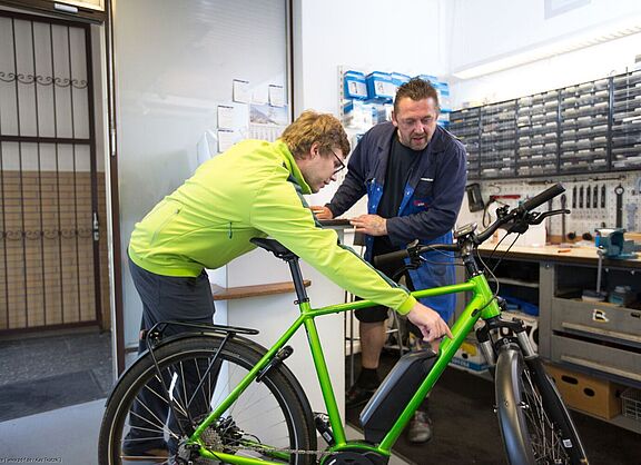 Ein Kunde zeigt dem Mechaniker in einer Werkstatt einen Defekt am Rad. 