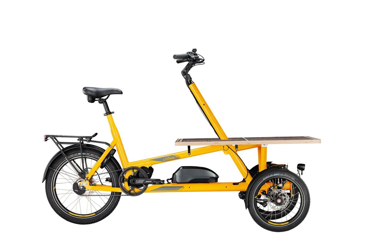 Gelbes Lastendreirad mit Transportfläche vor weißem Hintergrund. 